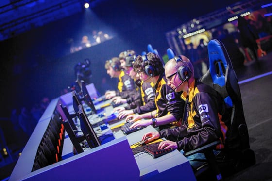 Equipe de eSports lado a lado na bancada de competição, de headset, durante uma partida.